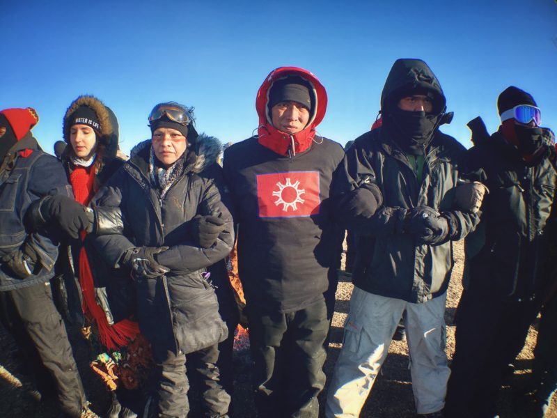 Protesters known as water protectors lock arms in preparation of a police raid during a Feb. 01 demonstration near the Standing Rock Sioux reservation. Photo by Jenni Monet.